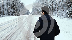 Camera pursues the man who walks on the winter road in the daytime.