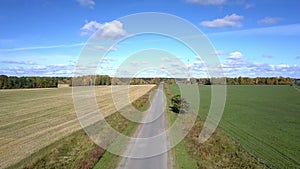 Camera rises above road between fields against blue sky