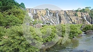 Camera shows brushwoods and rocks on foreground by Pongour waterfall