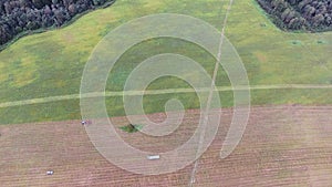 Camera shows large green and grey field with tractors, combines and cars on it.