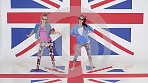 Camera shows rehearsal of two female dance performers on background of UK flag