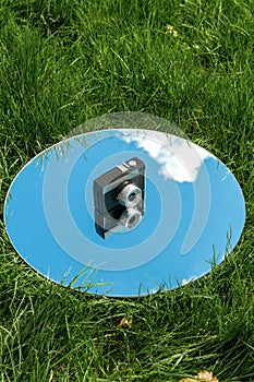 camera and sky reflection in round mirror on grass