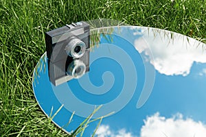 camera and sky reflection in round mirror on grass