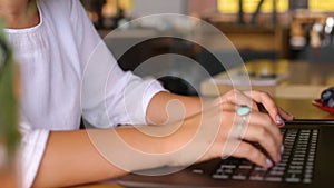 Camera slides around female freelancer's hands typing on laptop keyboard and rises to her face. Mixed race