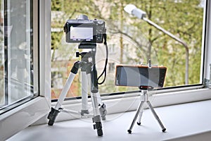 Camera and smartphone on tripods in front of an open window. Time lapse photography - smartphone vs camera