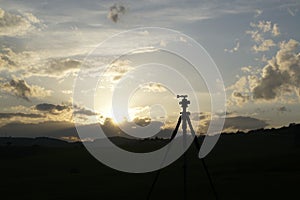 Camera stative silhouette on meadow during sunset.