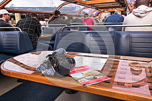 Camera on table with tour guide by interior seating inside a glass roofed sightseeing canal cruise trip boat for tourists