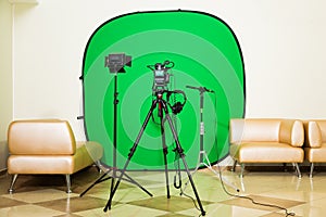 The camera on the tripod, led floodlight, headphones and a directional microphone on a green background. The chroma key