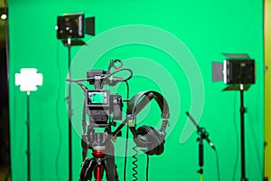 The camera on the tripod, led floodlight, headphones and a directional microphone on a green background. The chroma key