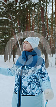 The camera zooms in on an adult happy woman in a blue ski suit in the forest