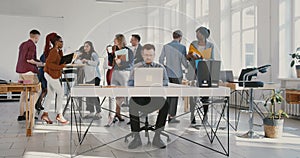 Camera zooms in on exhausted young businessman throwing paper documents in the air at busy modern office table RED EPIC.