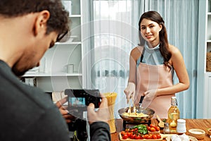 Cameraman recording to woman in chef influencer cooking spaghetti. Postulate.