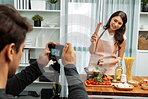 Cameraman recording to woman in chef influencer cooking spaghetti. Postulate.