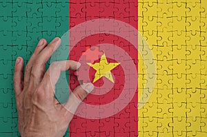 Cameroon flag is depicted on a puzzle, which the man`s hand completes to fold