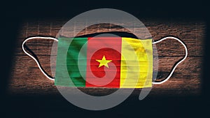 Cameroon National Flag at medical, surgical, protection mask on black wooden background. Coronavirus CovidÃ¢â¬â19, Prevent infection photo