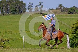 CAMINOS, CANELONES, URUGUAY, OCT 7, 2018: Gaucho riding a horse and waving the Uruguayan flag at a Festival in Uruguay