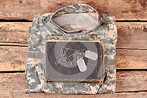 Camouflage army clothes, book, and dog tags on wood.