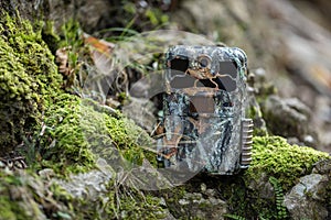 Camouflaged trail camera standing on a moss covered rocks in nature