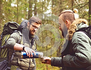 Camp, adventure, traveling and friendship concept. Man with a backpack and beard and his friend hiking in forest.