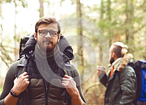 Camp, adventure, traveling and friendship concept. Man with a backpack and beard and his friend hiking in forest.