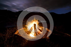 Camp fire beside lake and mountains