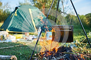 Camp fire and pot for food preparation with a defocussed tent in the background.