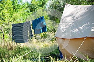 Camp tent on green grass on the trees background. Wet clothes drying on rope between the tents. Camping, tourist life