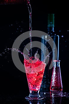 Campari and vodka with splashes on dark black background and bottles behind and liquid spilled on the glass