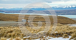 Camper van is driving on a deserted road in South Island, New zealand. In the background you can see the snow-covered mountains