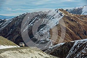 Camper van is driving on a deserted road in South Island, New zealand. In the background you can see the snow-covered mountains