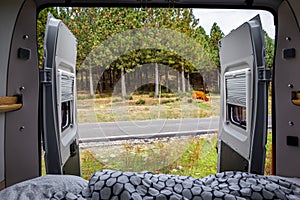 Camper van with opened back doors and bed with forest and meadow view, Spain.