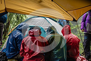 campers in rain jackets huddled under a tent canopy