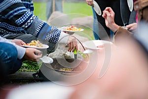 Campers sharing food cooked on sooty pot on campfire. People at survival camp