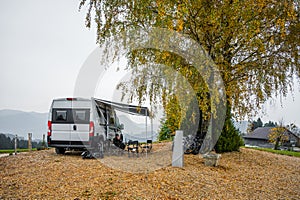 Campervan or motorhome parked in the countryside nature. Woman is drinking coffee in front of camper van motor home RV, parked