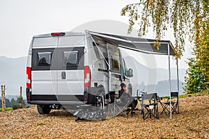 Campervan or motorhome parked in the countryside nature. Woman is drinking coffee in front of camper van motor home RV, parked