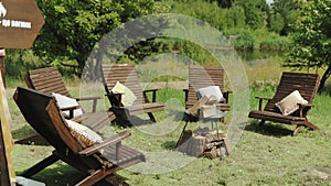 Campfire area, wooden chairs with small pillow on it around fire pit outside in nature in yard sunny day near small