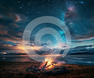 Campfire burning bright in field under starry night sky