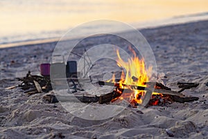 Campfire burns on the seashore next to waves during sunset