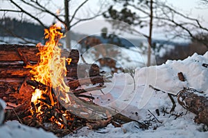 Campfire burns in the snow in the forest hill, on a background of snow covered trees and mountains campfire burning in cold winter