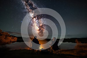 campfire crackling as two people sit on camping chairs, looking at the stars