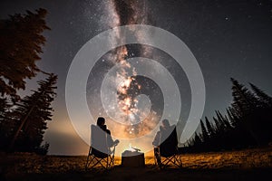 campfire crackling as two people sit on camping chairs, looking at the stars