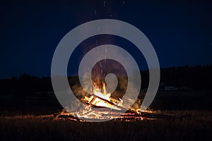 Campfire at night, with its soothing flickering flames and red and orange glow of the burning logs at dark night