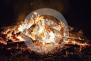 Campfire at night, with its soothing flickering flames and red and orange glow of the burning logs at dark night