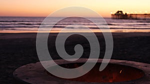 Campfire pit in California USA. Camp fire on twilight ocean beach, bonfire flame by sea water waves.