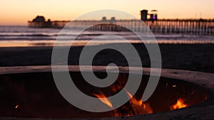 Campfire pit in California USA. Camp fire on twilight ocean beach, bonfire flame by sea water waves.