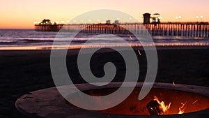 Campfire pit in California USA. Camp fire on twilight ocean beach, bonfire flame by sea water waves.