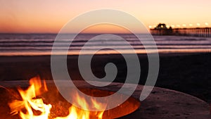 Campfire pit in California USA. Camp fire on twilight ocean beach, bonfire flame by sea water waves.