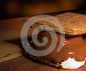 Campfire smore ready to eat on a wood table with orange light behind