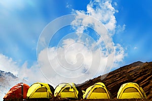 Campground in the mountains. Many yellow adn red tents against the blue sky with amazing clouds photo