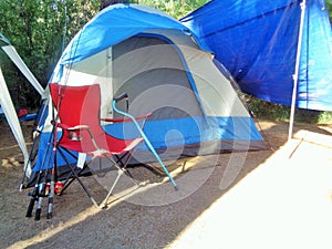 Campground Scene with a Tent, Walking Cane and Fishing Poles Leaning Against a Camp Chair